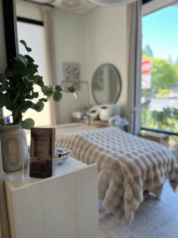 Skin Reserve Lab brochure beside eucalyptus, with the treatment room softly blurred behind.