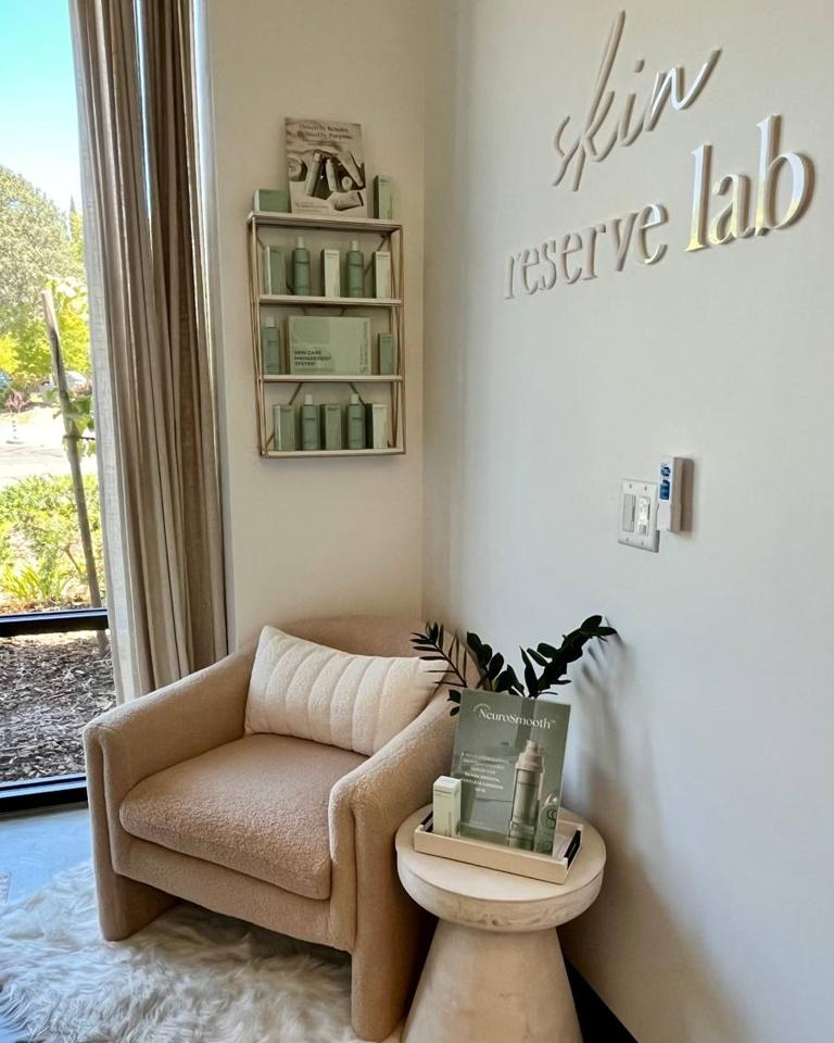 The skin reserve lab sign on the studio wall, beside a blush bouclé armchair and a shelf of Jan Marini skincare.