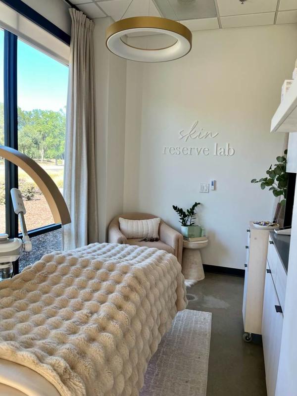 The treatment room: a bed under a plush cream throw, gold ring pendant light, the skin reserve lab sign and a reading chair.